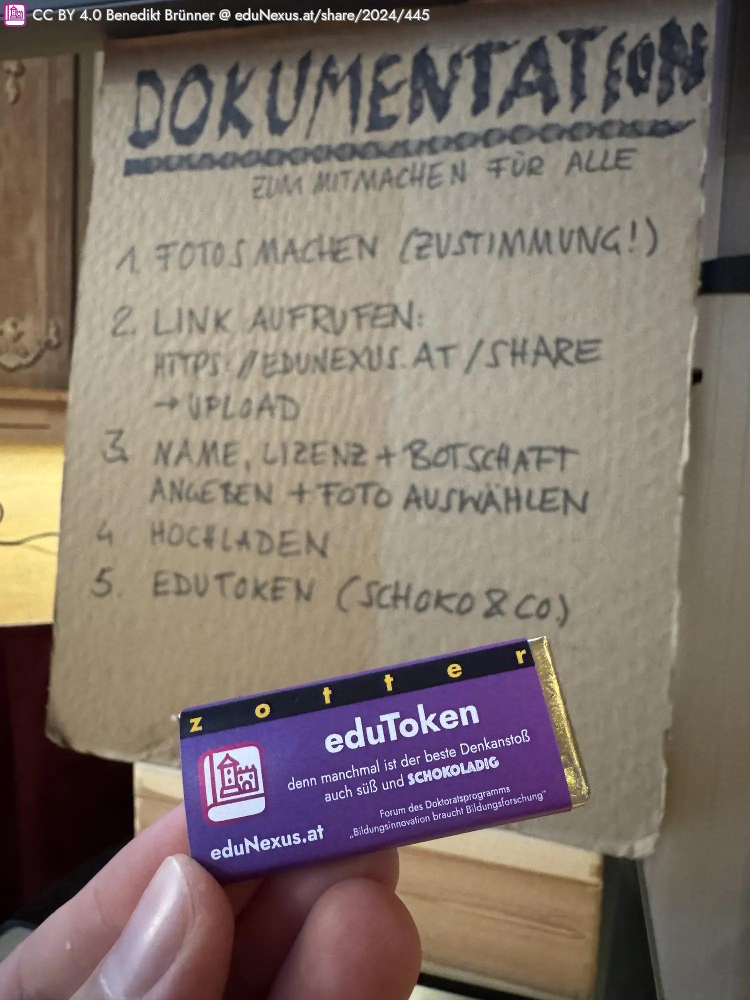 Dokumentationsanleitung auf einem Blatt Papier mit fünf Punkten; eine Hand hält eine Schokolade mit der Aufschrift „eduToken“ und dem Logo von eduNexus.