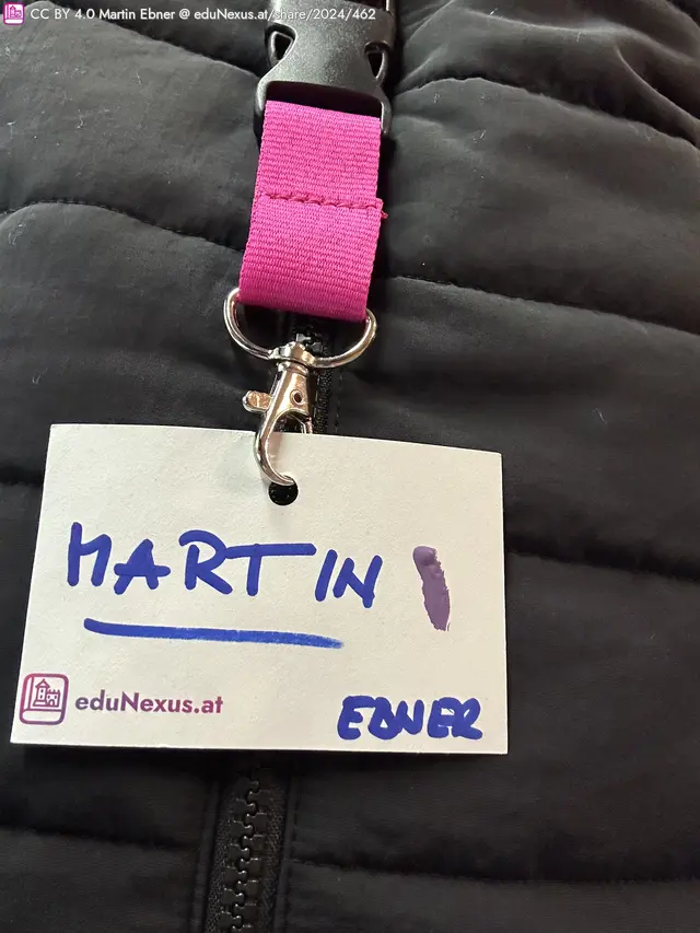 Schwarze Jacke mit einem Namensschild, das „MARTIN“ und „EBNER“ in blauer Schrift zeigt, befestigt mit einem pinken Band.