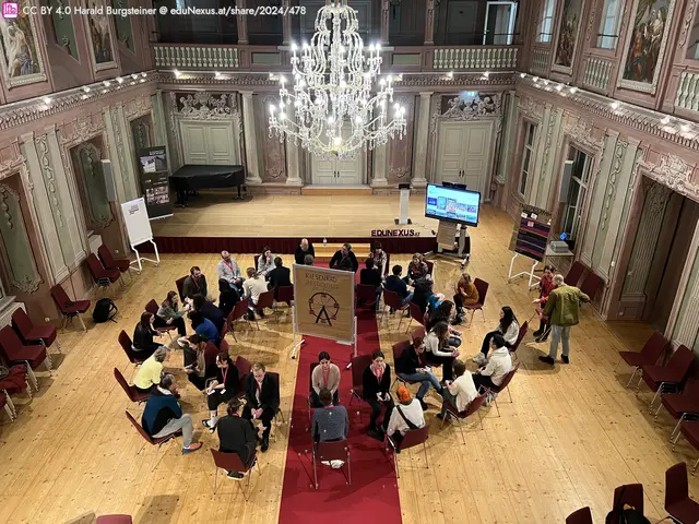 Runder Tisch mit Teilnehmern in einem eleganten Raum, umgeben von Stühlen, einem Kronleuchter und einer Leinwand im Hintergrund.