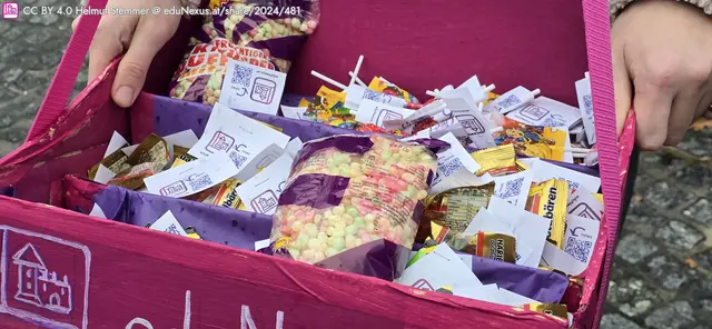 Eine pinke Kiste voller bunter Süßigkeiten, Tüten mit Popcorn und kleinen Päckchen mit Snacks.