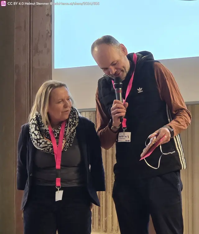 Erika und Martin auf einer Bühne, Erika mit blondem Haar und Schal, Martin mit Mikrofon und dem Lebkuchenherz.