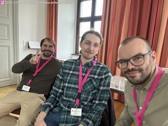 Drei Männer sitzen in einem Raum mit roten Vorhängen. Jeder trägt ein Namensschild mit einer pinken Lanyard. Der Mann links macht ein Peace-Zeichen.