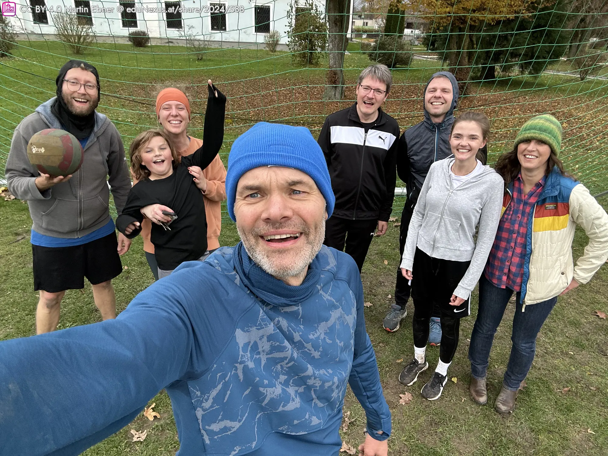 Gruppe von sieben Personen in sportlicher Kleidung, lächelnd und posierend vor einem Fußballtor im Freien.