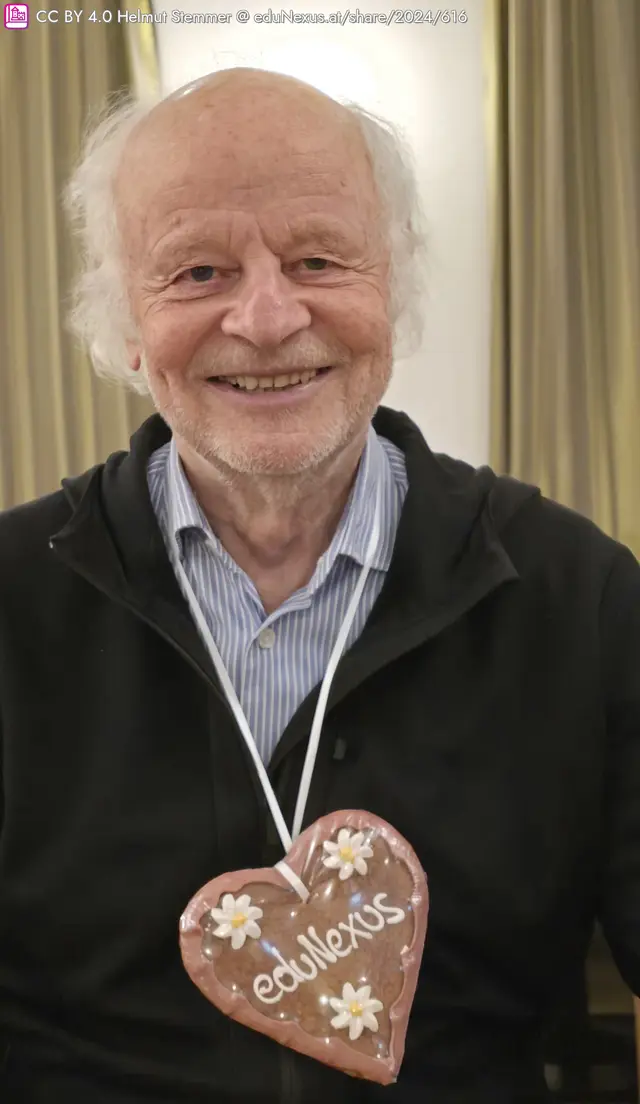 Lächelnder älterer Mann (Prof. Mayr) mit grauen Haaren, trägt einen schwarzen Pullover und hat ein großes herzförmiges Lebkuchenherz mit der Aufschrift „edulexus“ um den Hals.