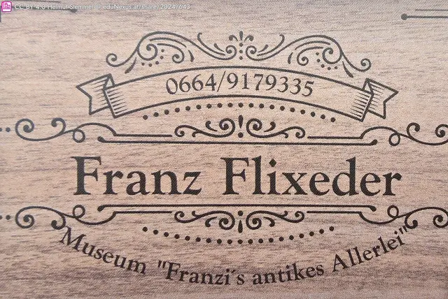 Holztextur mit dem Namen „Franz Flixeder“, Telefonnummer „0664/9179335“ und dem Schriftzug „Museum ‚Franzi’s antikes Allerlei'“.