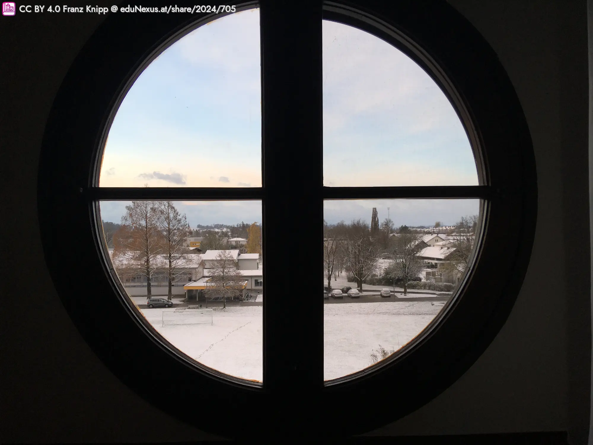 Runder Fensterrahmen mit Blick auf verschneite Landschaft und Häuser.